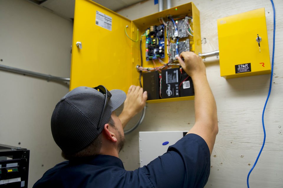 Technician working inside an open wall-mounted control enclosure.